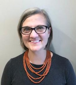 professor wearing a black shirt with an orange necklace standing in front of a white backdrop